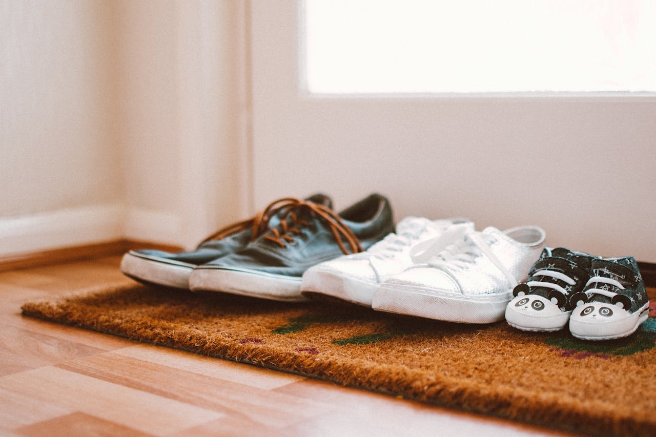 A photo of three pairs of shoes at the front door of a house.